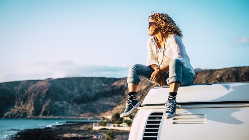 Travel concept with independent people enjoyig the outdoor leisure activity and wanderlust life lifestyle - woman sit down on the roof of a old nice vintage camper van